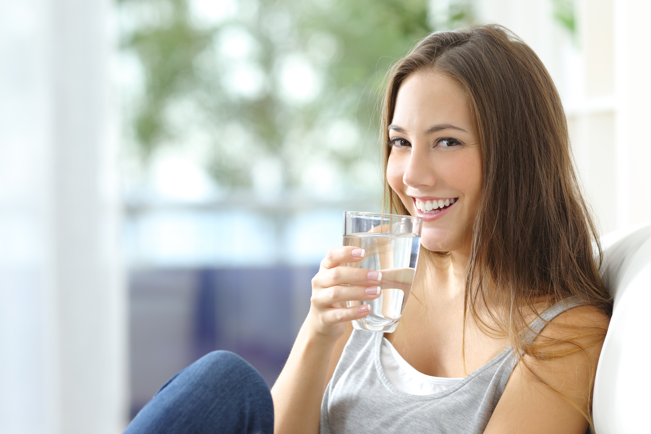 mujer tomando agua sentada en un sofá